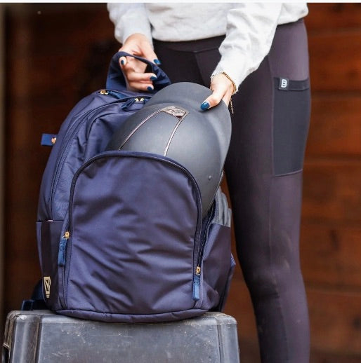 Woman placing an equestrian riding helmet into a Veltri Sport Delaire backpack before heading to the barn.