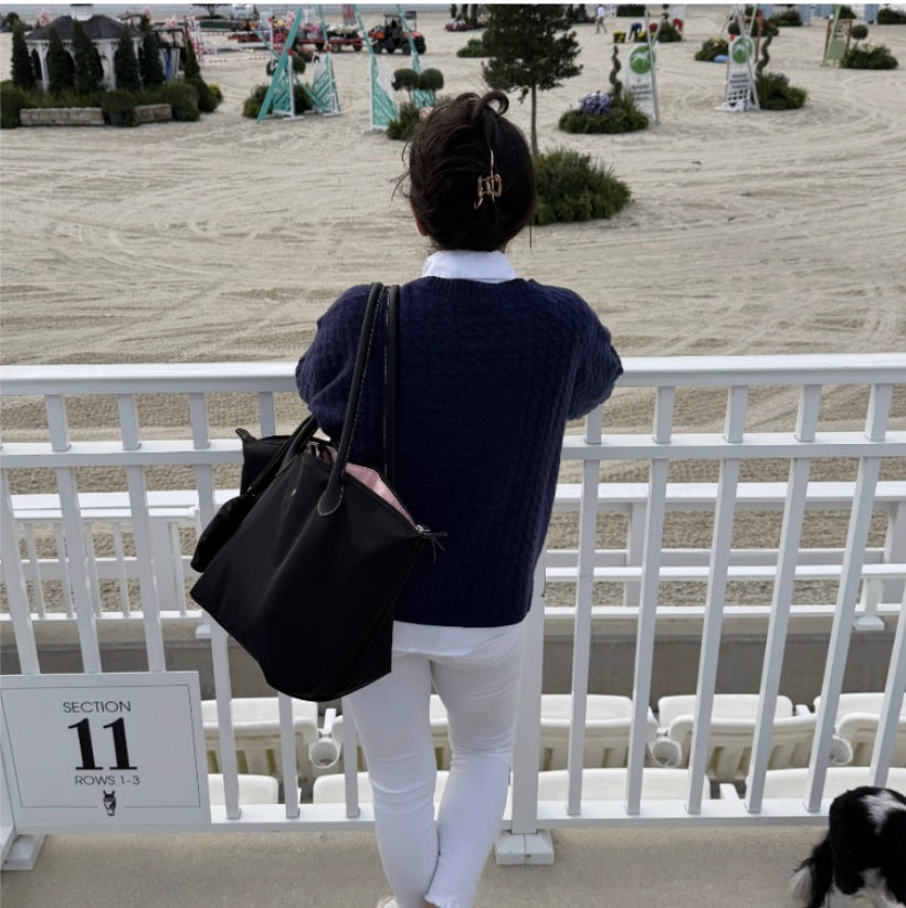 A woman carrying the Veltri Sport Campus Tote overlooking an equestrian show arena before the vent starts.