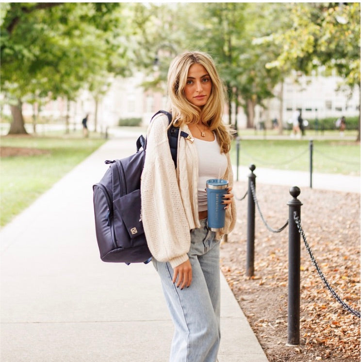 College girl holding water bottle walking on campus with Veltri Sport Delaire backpack in navy on.
