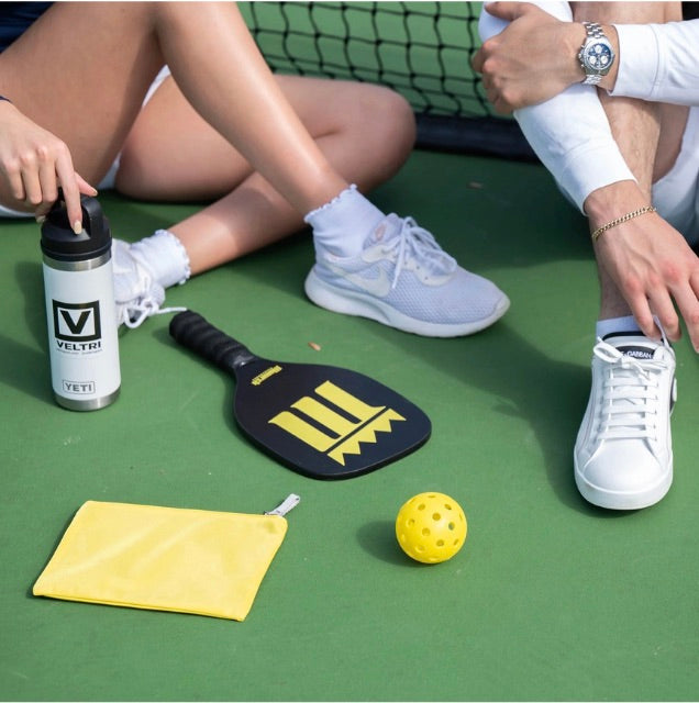 Veltri Sport Darius Zip Pouch on tennis court with other tennis accessories.
