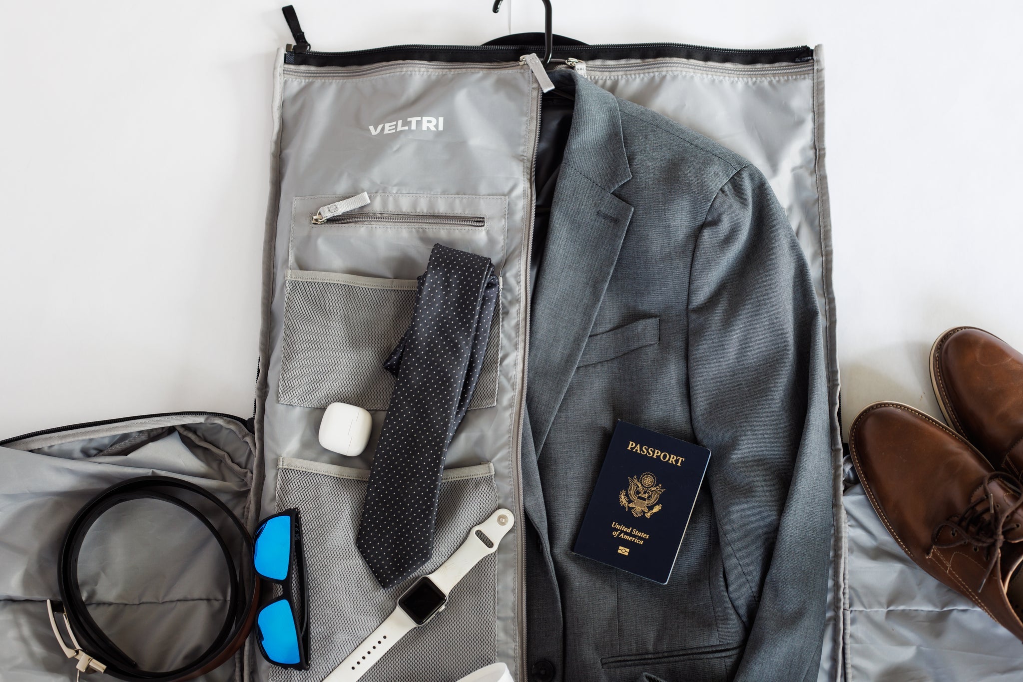 Interior view of Veltri Sport's Ellis Garment Duffle with all the travel belongings a man may use including a suit, tie, belt shoes, and passport