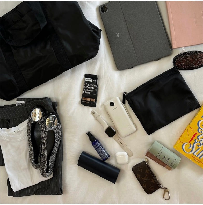 Veltri Sport Newport Tote in black laid against white background among business outfit and other work necessities.