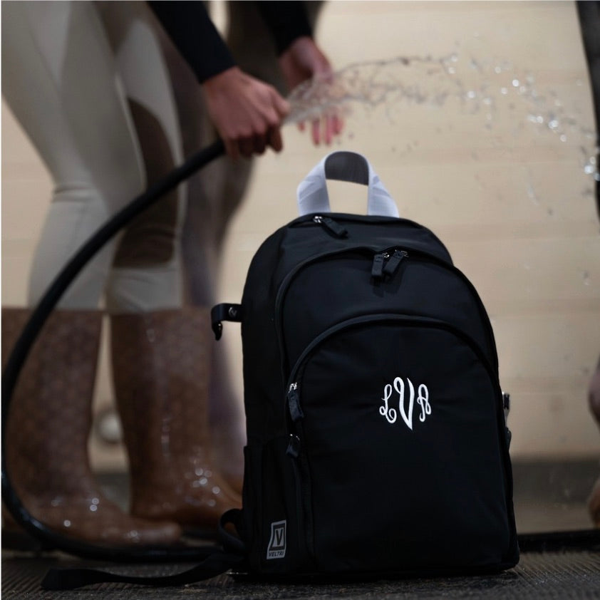 Equestrian cleaning her Veltri Sport embroidered Grande Backpack in black with a hose.