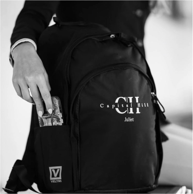 Women putting phone into phone pocket of Veltri Sport embroidered Delaire Backpack in black.