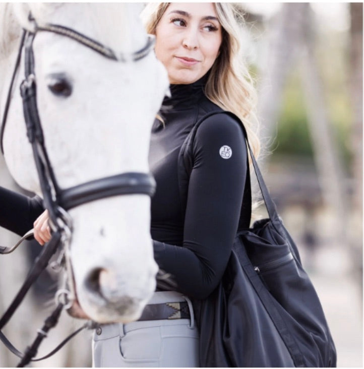 A horse mom is holding a white horse while carrying her Veltri Sport Newport Tote in black which has all of her and her daughter's horse show essentials.  