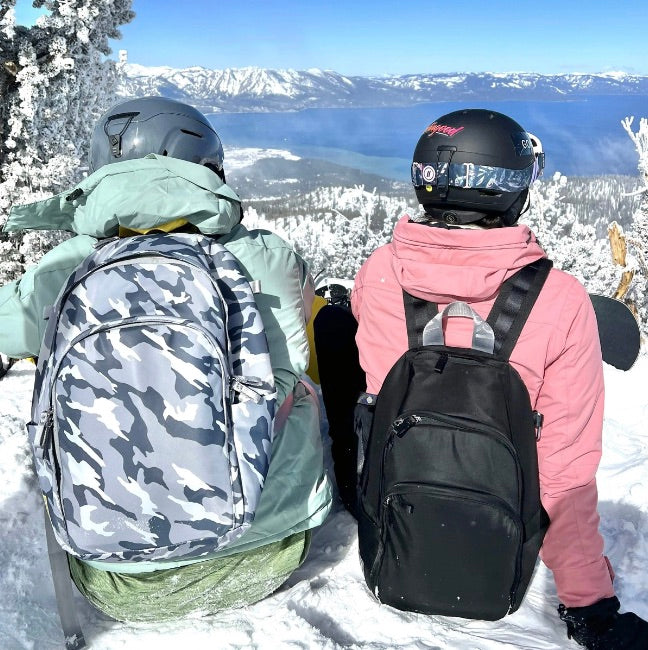 Two snowboarders enjoying a mountain overlook with snowboards and Veltri Sport Delaire backpacks after a day on the slopes.