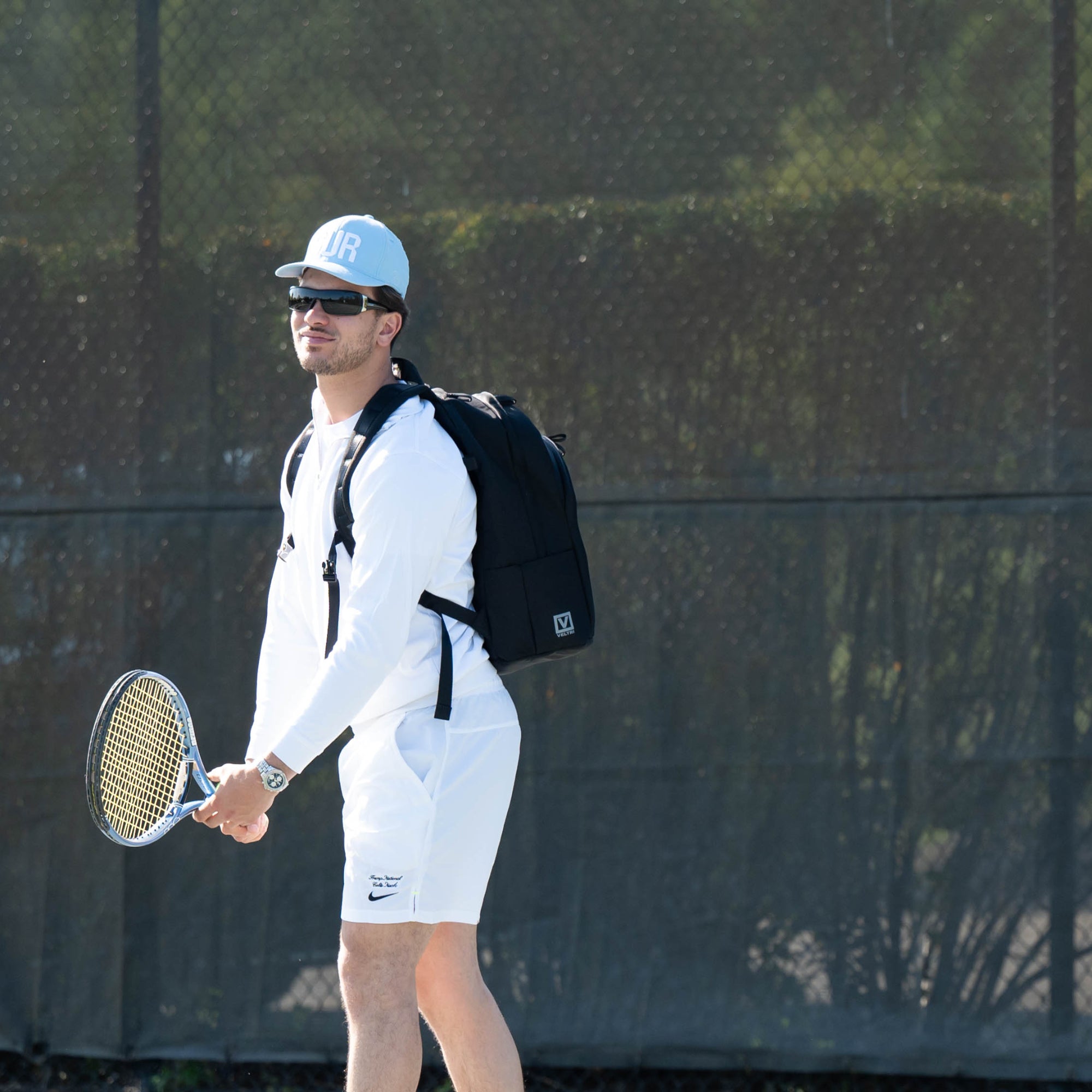 Veltri Sport Grande Backpack in Black worn by a man holding a tennis racket on an outdoor tennis court.
